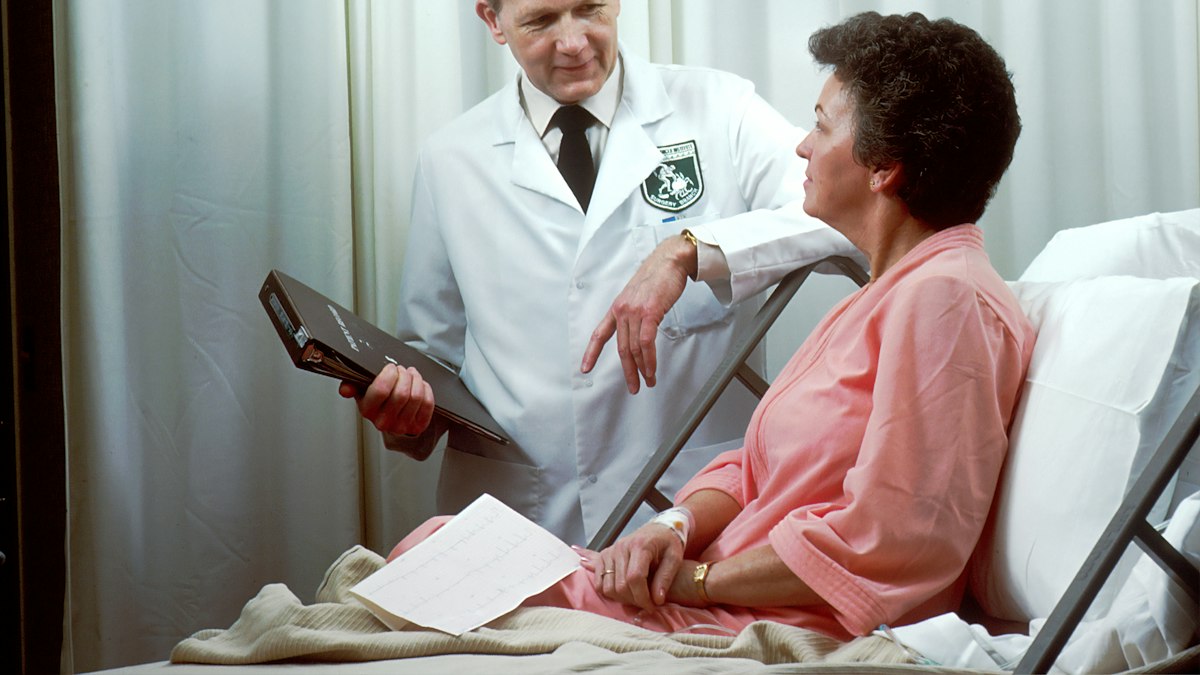 A doctor talking with an older patient sitting up in a hospital bed