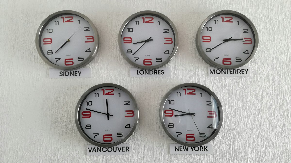 Five wall clocks showing the time in Sydney, London, Monterrey, Vancouver, and New York