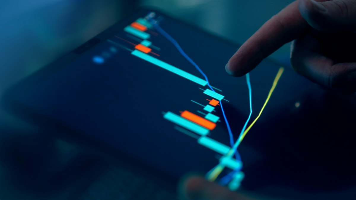 A finger touching a candlestick chart on a tablet screen