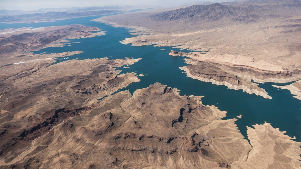 Aerial view of a desert reservoir with a pale band of exposed rock along its shoreline